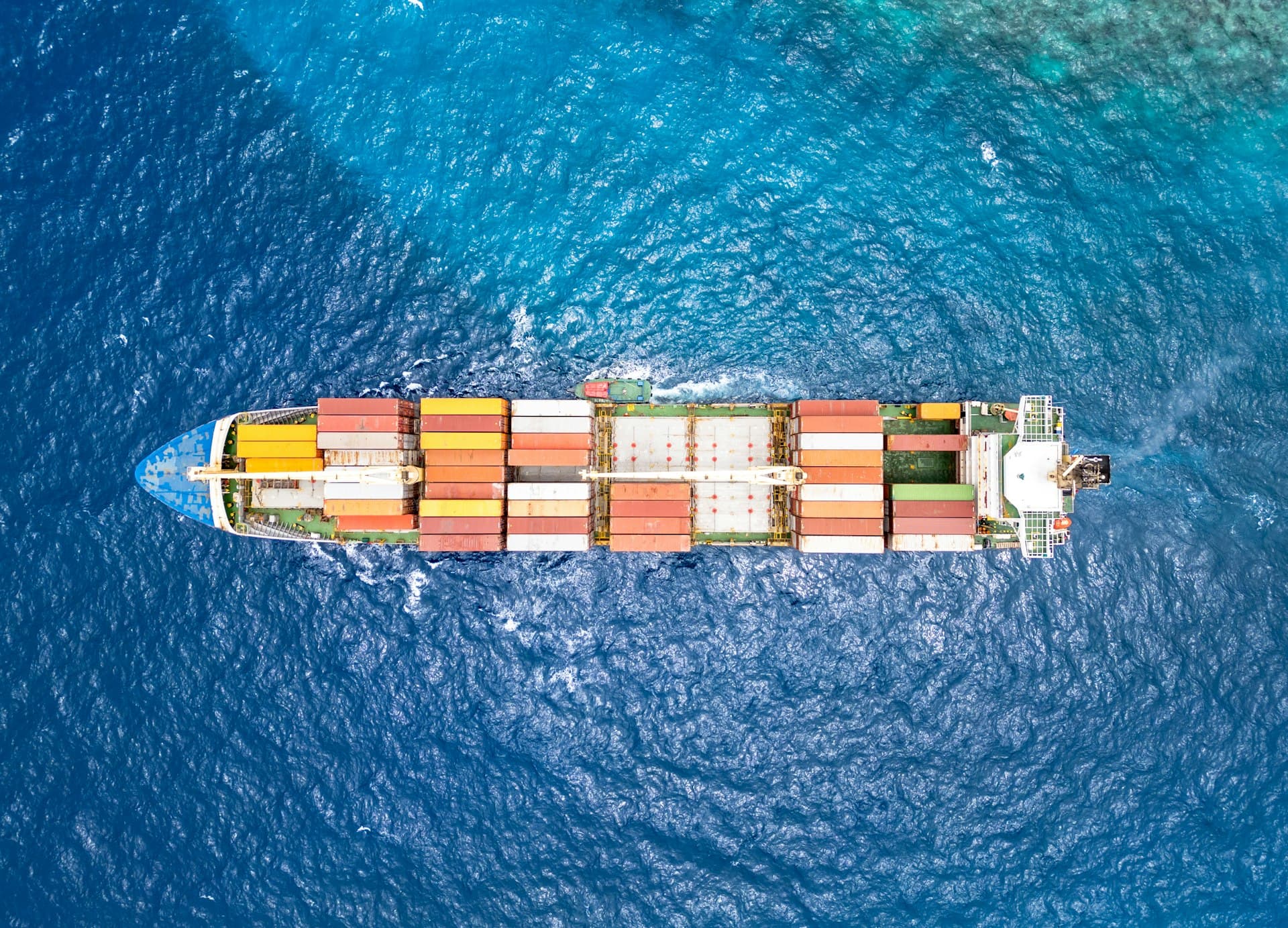 Aerial top-down view of a container ship loaded with colorful shipping containers crossing deep blue ocean water